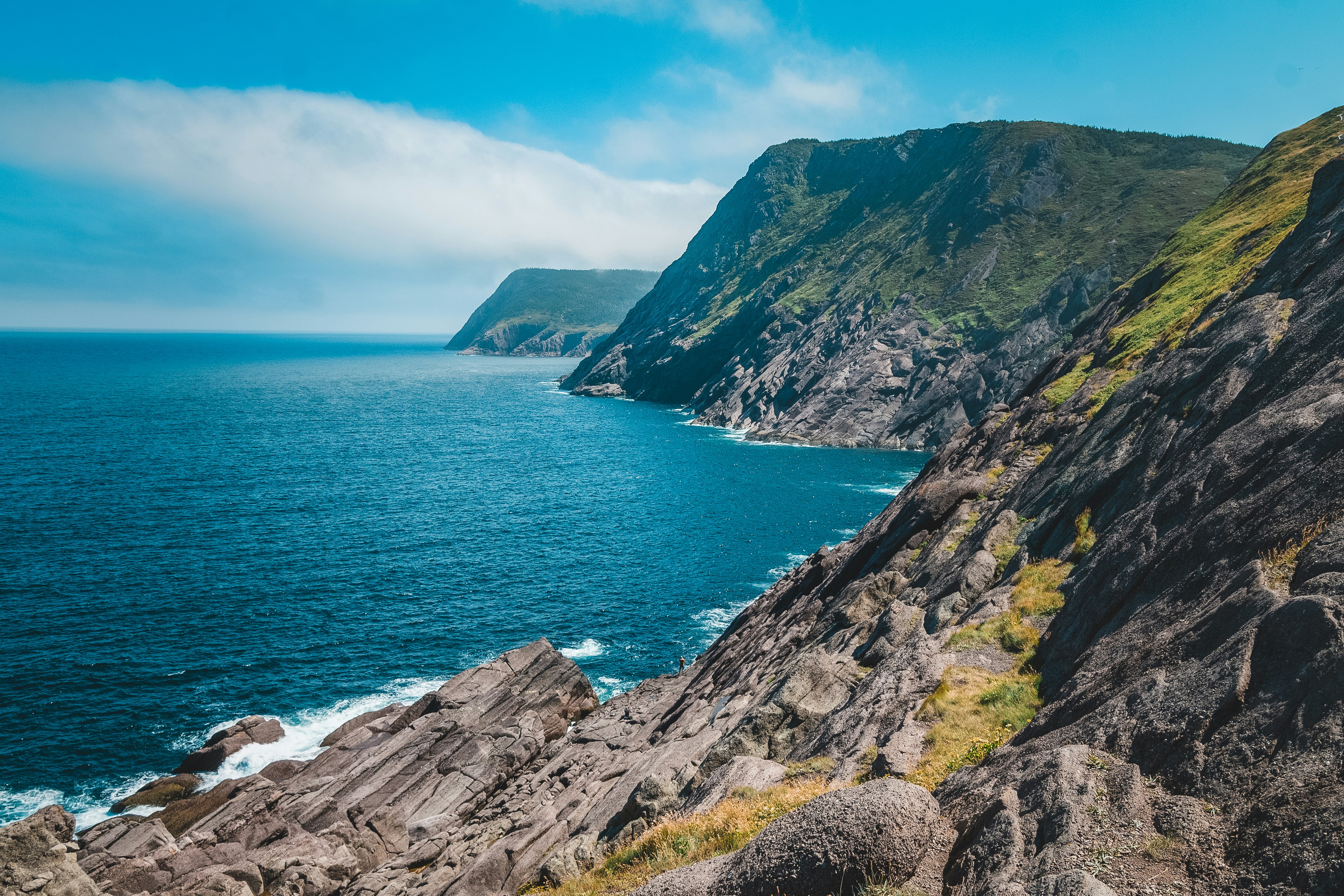 green and brown mountain beside body of water under blue sky during daytime